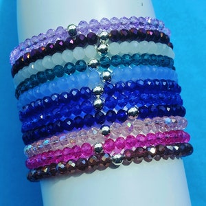 May include: A stack of colourful crystal bracelets with silver beads. The bracelets are made of various shades of purple, blue, pink, and teal.