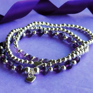May include: Three layered bracelets with silver beads and amethyst stones. The bottom bracelet has a silver heart charm.