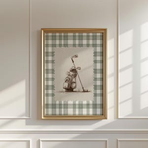 Può includere: Un'opera d'arte incorniciata a tema golf. L'opera presenta uno schizzo di una sacca da golf con mazze. L'opera è ambientata su uno sfondo beige con un bordo a scacchi verdi e bianchi, il tutto all'interno di una cornice dorata. L'opera è montata su un muro bianco.