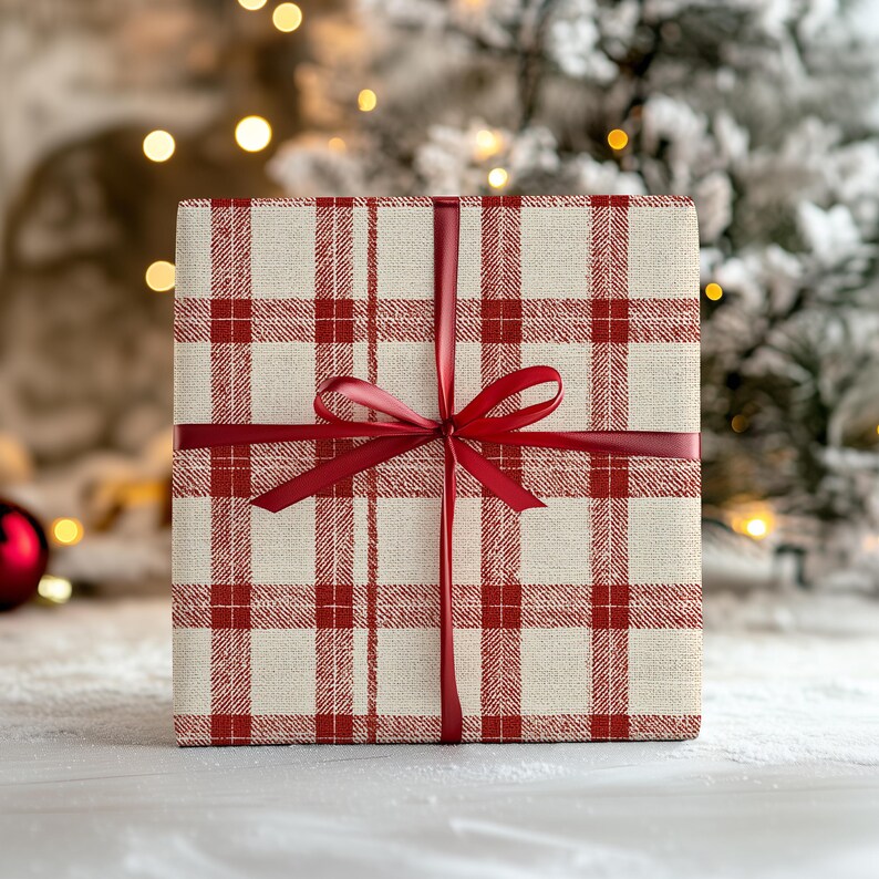 K&ouml;nnte beinhalten: Ein quadratischer Geschenkkarton, verpackt in cremefarbenem Papier mit einem roten Karomuster. Die Box ist mit einem roten Satinband und einer Schleife gebunden. Der Hintergrund zeigt einen verschwommenen Weihnachtsbaum und Lichter.