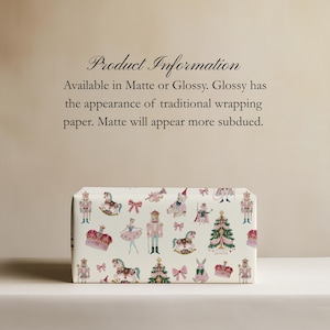 May include: Wrapping paper featuring a repeating pattern of nutcrackers, ballerinas, rocking horses, Christmas trees, crowns, and bows in pink, green, and gold on a cream background. Text reads: Product Information Available in Matte or Glossy.