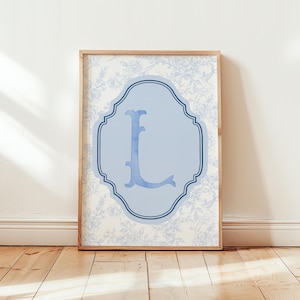 May include: Framed wall art featuring a light blue letter "L" within a decorative light blue frame. The background showcases a floral pattern in light blue and white, all set within a natural wood frame.