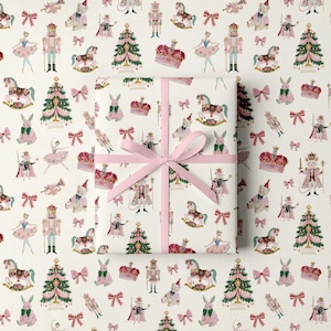 May include: A rectangular gift box wrapped in white paper featuring a repeating pattern of Christmas trees, nutcrackers, ballerinas, rocking horses, crowns, and pink bows, tied with a light pink ribbon centered in a cross pattern.