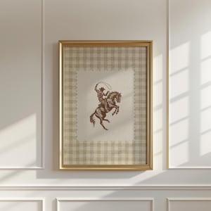 Puede incluir: Obra de arte enmarcada con una ilustración en tonos sepia de un vaquero a caballo, con un lazo en la mano. La obra está sobre un fondo a cuadros beige y blanco, enmarcada en un marco dorado. Tema: Western.