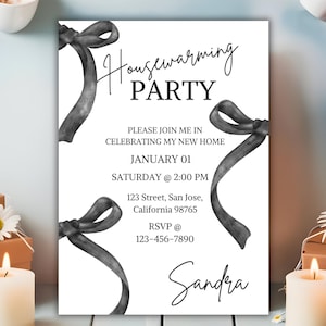 May include: Black and white housewarming party invitation with a handwritten font. The invitation features a decorative ribbon design and the text "Housewarming Party", "Please join me in celebrating my new home", "January 01", "Saturday @ 2:00 PM", "123 Street, San Jose, California 98765", "RSVP @ 123-456-7890", and "Sandra".