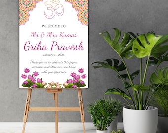 May include: A white sign with pink and orange floral borders and a pink Om symbol. The sign reads "Welcome to Mr. & Mrs. Kumar Griha Pravesh January 01, 2024 Please join us to celebrate this joyous occasion and bless our new home with your presence."