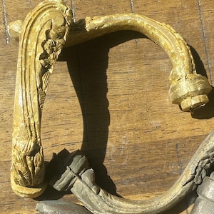 May include: A pair of ornate, gold-toned metal door handles with intricate floral designs. The handles are in the shape of a curved 'D' with a decorative end.