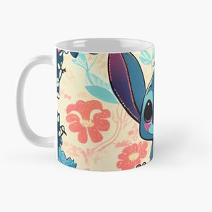 May include: White ceramic mug with a colorful floral pattern and a cartoon blue alien character with pink accents. The alien is smiling and has large eyes.