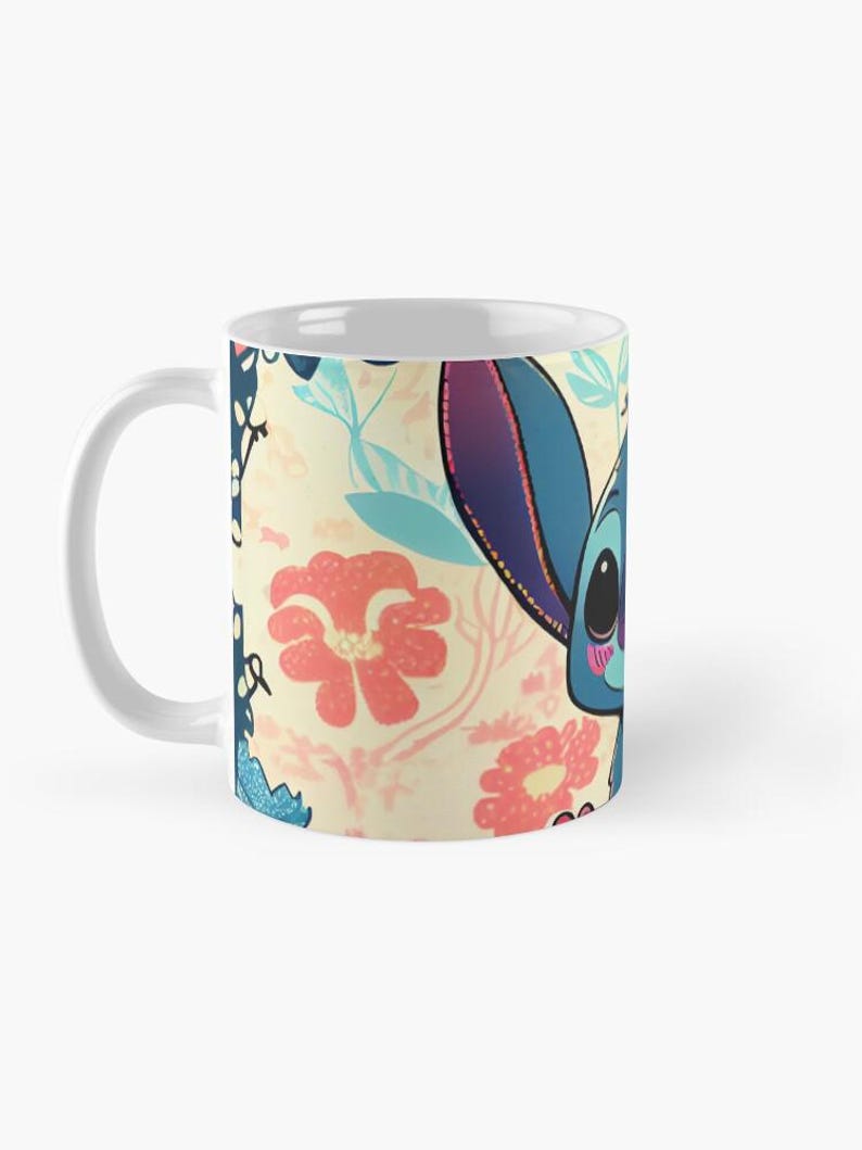 May include: White ceramic mug with a colorful floral pattern and a cartoon blue alien character with pink accents. The alien is smiling and has large eyes.