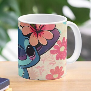May include: A white ceramic mug with a colorful design featuring a cartoon Stitch character with pink flowers. The background is a light pink with a floral pattern.