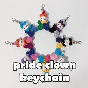 May include: A collection of colorful, crocheted clown keychains arranged in a circular pattern. Each keychain features a unique color scheme, with the text "pride clown keychain" in the center.