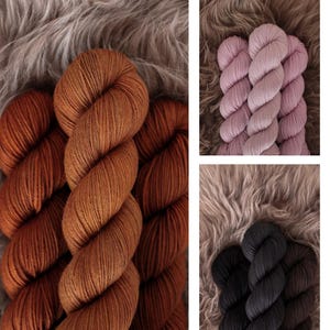 May include: Three skeins of yarn in different colors: a deep orange, a light pink, and a dark charcoal. The yarn is arranged in a spiral shape on a fuzzy brown surface.