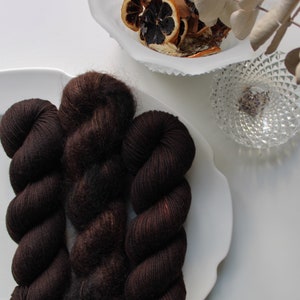 May include: Three skeins of dark brown yarn, arranged in a spiral on a white plate. The yarn is soft and fluffy, and the color is a rich, deep brown.