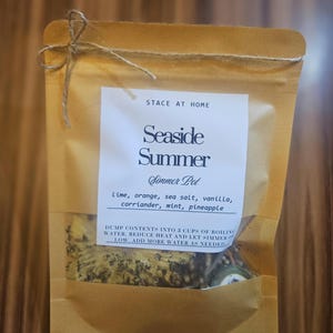 Puede incluir: Una bolsa de papel marrón con una ventana transparente que contiene ingredientes secos. La etiqueta dice Stace at Home, Seaside Summer, Simmer Pot, e incluye lima, naranja, sal marina, vainilla, cilantro, menta y piña. Con un lazo de yute.