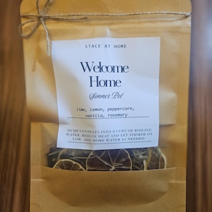 Könnte beinhalten: Ein brauner Papierbeutel mit Sichtfenster, der getrocknete Früchte und Kräuter enthält. Das Etikett lautet: STACE AT HOME, Welcome Home, Simmer Pot, Lime, Lemon, peppercorn, vanilla, rosemary. DUMP CONTENTS INTO 3 CUPS OF BOILING WATER.