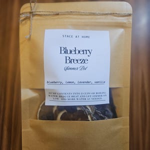 Könnte beinhalten: Ein brauner Papierbeutel mit Sichtfenster, der getrocknete Früchte und Kräuter enthält. Das Etikett zeigt STACE AT HOME, Blueberry Breeze Simmer Pot, blueberry, Lemon, Lavender, vanilla sowie Anweisungen für 3 Tassen kochendes Wasser.