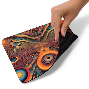 Puede incluir: Una alfombrilla de ratón con un diseño abstracto colorido y un respaldo de goma negro. El diseño presenta una variedad de formas y colores, incluyendo naranja, amarillo, azul y rojo.