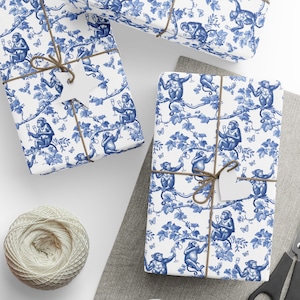 Puede incluir: Regalos envueltos con un patrón de toile de mono azul y blanco. Los regalos están atados con hilo y tienen etiquetas en forma de estrella. También se ven una madeja de hilo y unas tijeras. El papel de regalo presenta monos, vides y mariposas.