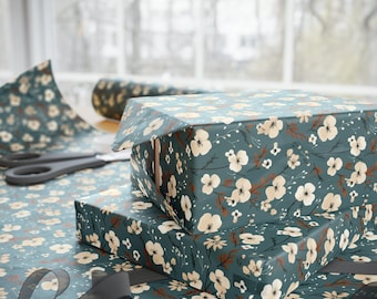 May include: Two gift boxes wrapped in teal blue wrapping paper with a white floral pattern. The boxes are stacked on top of each other and are sitting on a table covered in the same wrapping paper.