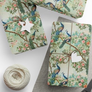 Pode incluir: Duas caixas de presente embrulhadas em papel estampado verde e branco com pavões e rosas cor-de-rosa. As caixas são amarradas com barbante e decoradas com formas de estrela e coração brancas.