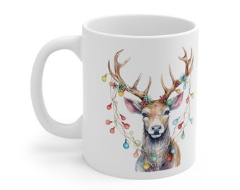 May include: White ceramic mug with a watercolor illustration of a deer with colorful Christmas lights wrapped around its antlers.