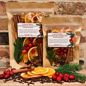 May include: Two clear pouches of Christmas simmering stovetop potpourri containing dried orange slices, cinnamon sticks, cranberries, and evergreen sprigs. The labels feature the text: CHRISTMAS SIMMERING STOVETOP POTPOURRI, UVALDE, TX, and a website.