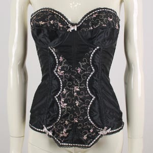 May include: Black strapless corset with pink floral embroidery and delicate lace trim. Features small pink bows and a structured bodice. A vintage-inspired lingerie piece.