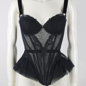 May include: Black corset with a sweetheart neckline and a peplum hem. The bodice features lace detailing and boning, with velvet straps. The corset is displayed on a mannequin.
