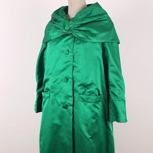May include: A long, emerald green satin coat with a large, rounded collar and button closure. The coat features two front pockets and a matching fabric-covered button detail. The coat is displayed on a mannequin.