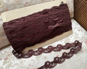 May include: A roll of burgundy lace trim with a scalloped edge. The lace is delicate and intricate, with a floral pattern.
