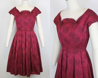May include: A vintage red dress with a black floral pattern. The dress has a scoop neckline, short sleeves, and a full skirt. It is made of a smooth, silky fabric.