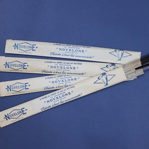 May include: Four white cardboard boxes with blue text and a blue logo that reads "NOVELONE". The boxes are stacked on top of each other and have a blue and white illustration of a person swinging a golf club. The text on the boxes reads "La valeur du corset est dans son balencage" and "Réside à tous les mouvements!"