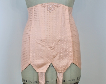 May include: A peach-colored, vintage-style garter belt with a delicate floral design and four adjustable straps. The garter belt is on a mannequin and has a textured, diamond-shaped pattern.