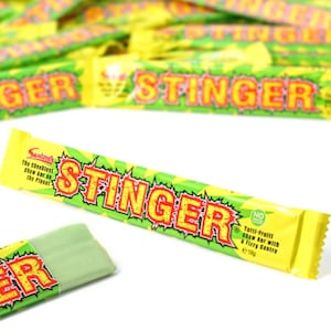 May include: A yellow and green candy bar wrapper with the text "STINGER" in red and yellow letters. The wrapper says "The cheekiest chew bar on the planet" and "Tutti-fruiti chew bar with a fizzy centre".