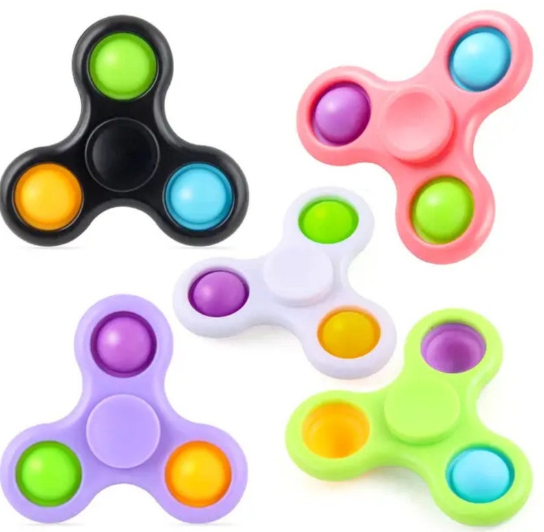 Może przedstawiać: Pięć spinner&oacute;w fidget w r&oacute;żnych kolorach: czarny, r&oacute;żowy, biały, fioletowy i zielony. Każdy spinner ma pięć kolorowych, okrągłych guzik&oacute;w z wgłębieniami.