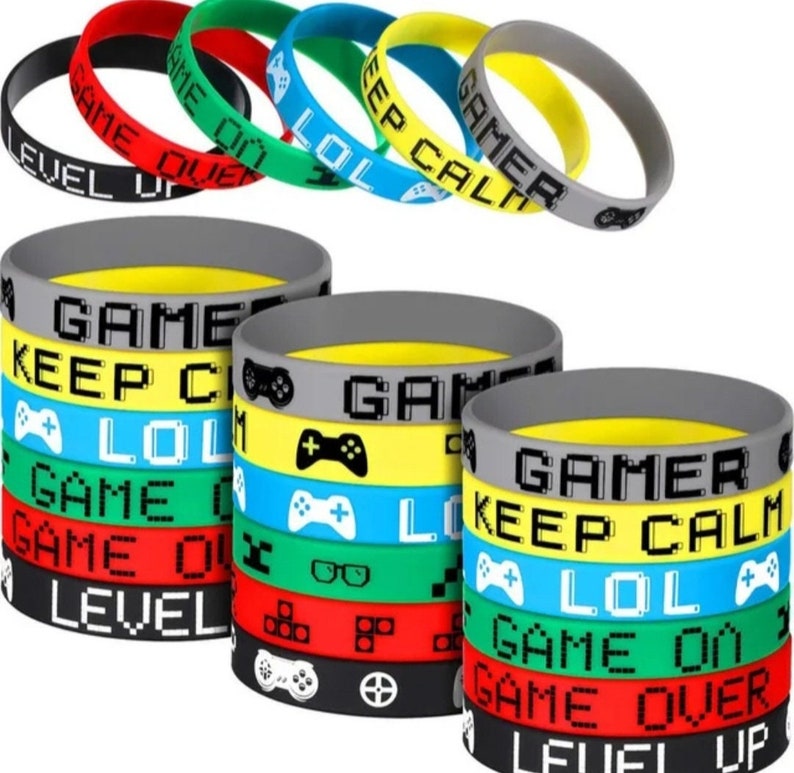 May include: A set of 10 colourful silicone bracelets with gamer-themed text and graphics. The bracelets feature phrases like "Game Over", "Level Up", "Keep Calm", "Gamer", and "LOL".