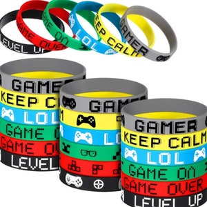 Może przedstawiać: Zestaw 10 kolorowych silikonowych bransoletek z motywami gier i napisami. Bransoletki zawierają takie frazy jak "Game Over", "Level Up", "Keep Calm", "Gamer" i "LOL".