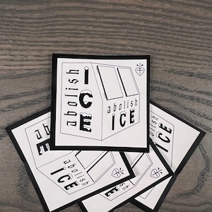 May include: Several square stickers with a black border and a black and white graphic. The graphic shows the words "abolish ICE" in a stylized font, alongside an illustration of a building. A small heart symbol is also present.