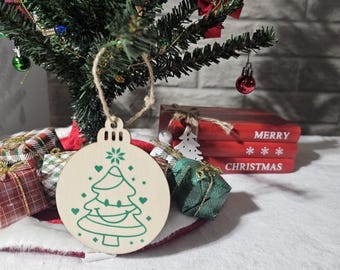 May include: A wooden Christmas tree ornament with a green tree design and white hearts. The ornament is hanging from a string and is in front of a small artificial Christmas tree.