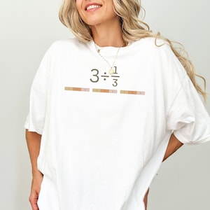 May include: White oversized t-shirt with the text "3 ÷ 1/3" printed on the front. The text is in brown and the shirt has a relaxed fit.