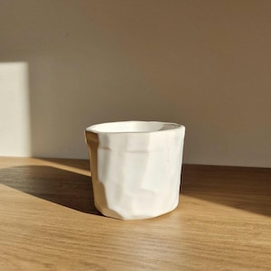 May include: White ceramic planter with a textured, geometric design. The planter is sitting on a wooden surface.