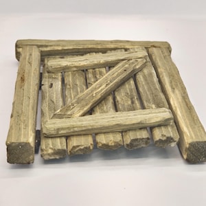 Può includere: Una piccola porta di legno con una traversa di legno diagonale. La porta è in legno invecchiato e ha un aspetto rustico.