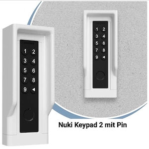 May include: A white rectangular electronic keypad with a black central panel featuring numerical buttons from one to nine and a back arrow symbol. The device includes a circular button at the bottom and is labeled Nuki Keypad 2 mit Pin.