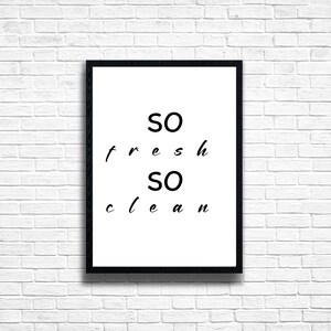 Könnte beinhalten: Gerahmter Druck mit den Worten "SO fresh SO clean" in schwarzer Schrift auf weißem Hintergrund. Der schwarze Rahmen hängt an einer weißen Backsteinmauer.