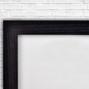 Op de afbeelding: Een zwarte houten fotolijst met een witte passe-partout. De lijst is tegen een witte bakstenen muur.