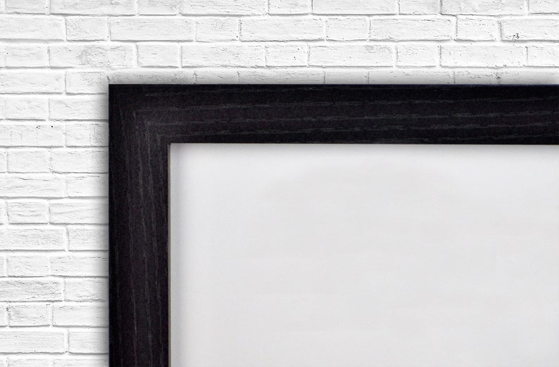 Op de afbeelding: Een zwarte houten fotolijst met een witte passe-partout. De lijst is tegen een witte bakstenen muur.