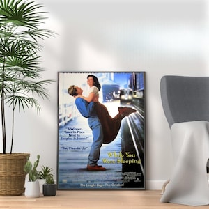 Può includere: Un poster del film per la commedia romantica "While You Were Sleeping" con Sandra Bullock e Bill Pullman. Il poster ha uno sfondo bianco con un treno blu e bianco sullo sfondo. Il testo "The Laughs Begin This October!" è in fondo al poster.