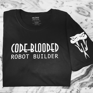 Peut inclure: T-shirt noir avec un texte blanc qui dit "(CODE-BLOODED) ROBOT BUILDER" et un graphique de serpent blanc sur la manche.