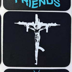May include: Black sticker featuring a white graphic of a figure on a cross, with machine guns replacing the crossbeams. The word "FRIENDS" is printed in turquoise above the image.
