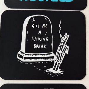 May include: Black sticker with a white illustration of a tombstone and a skeleton hand. The tombstone reads "GIVE ME A FUCKING BREAK". A humorous and edgy design.
